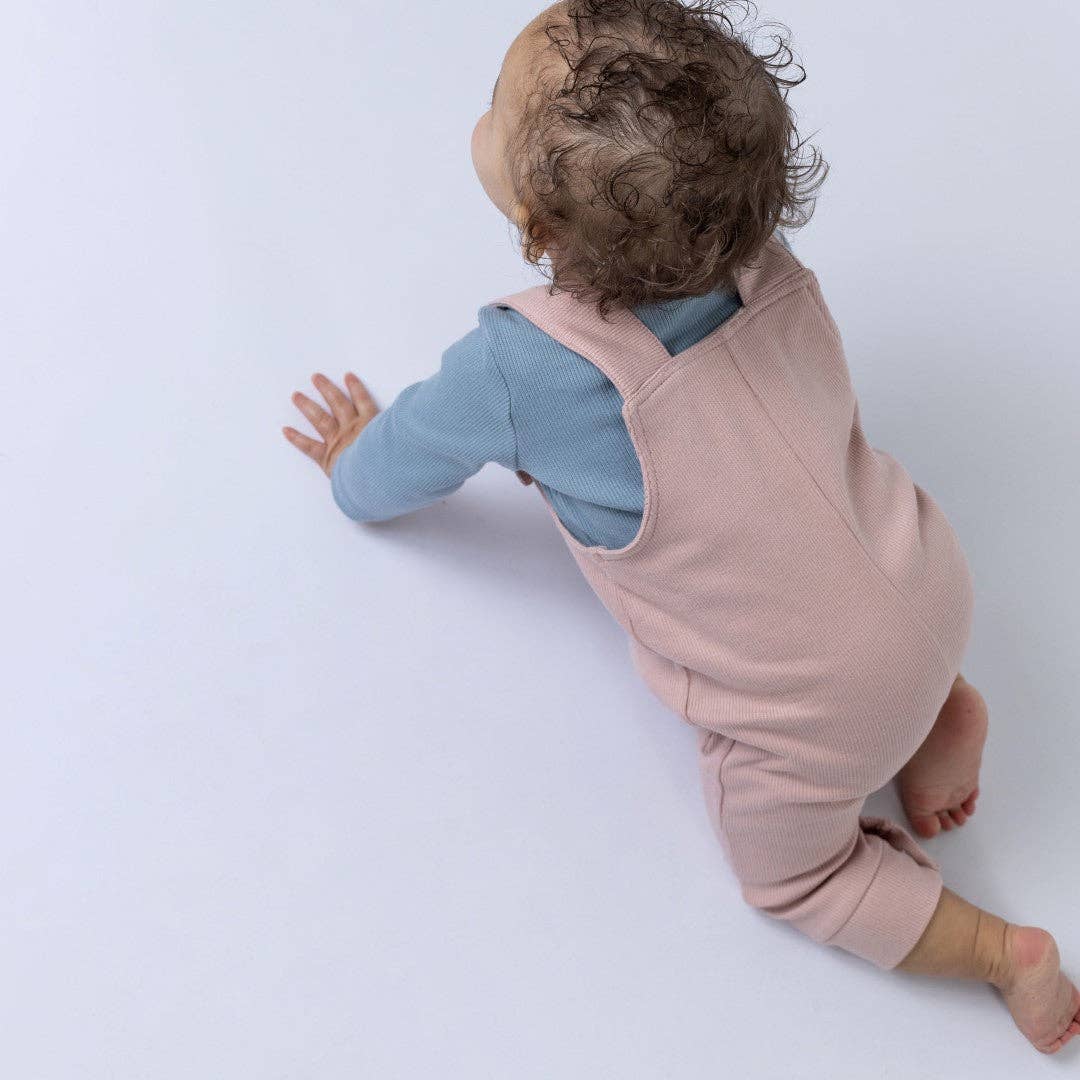 Baby in pink dungaree and blue shirt on a white background