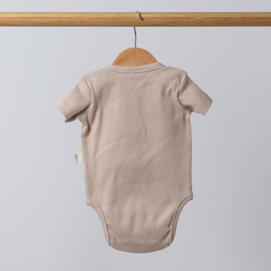 Beige baby bodysuit on a wooden hanger against a light gray background