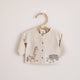 Baby cardigan with animal illustrations on a hanger against a light background